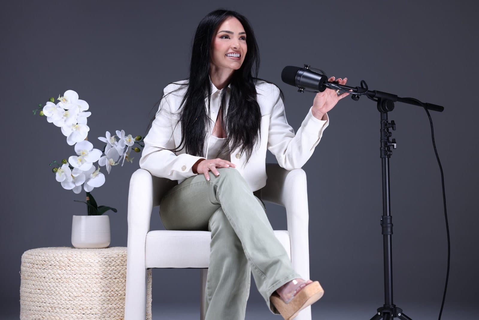 Taneth laughing in a white blazer beside a podcast mic